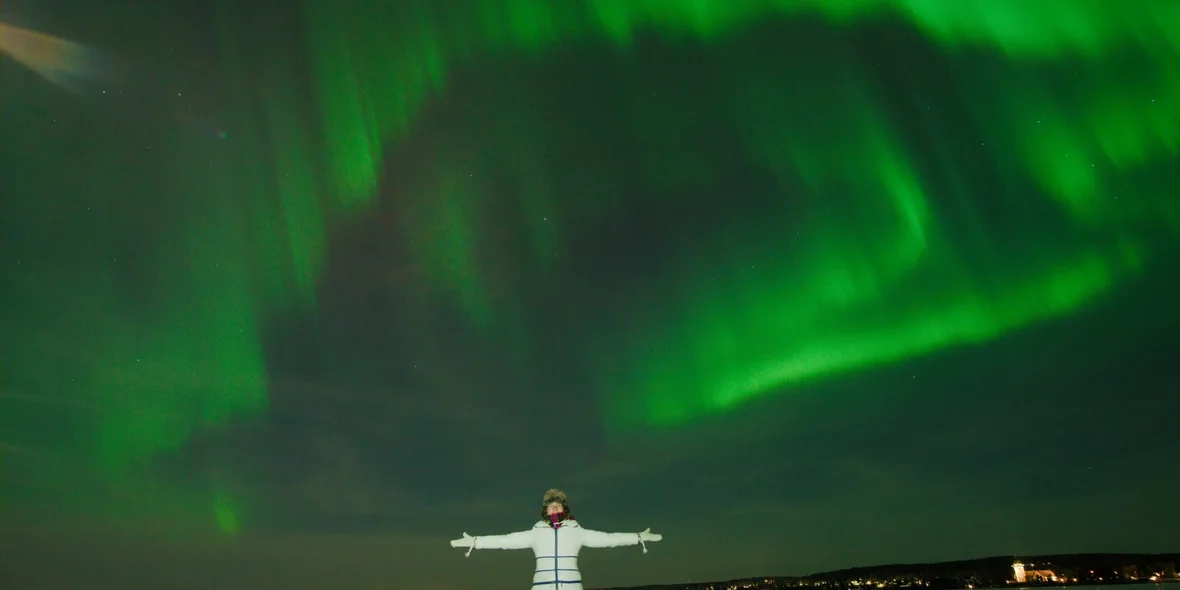 A photo of a girl with the northern lights in Sweden in the background