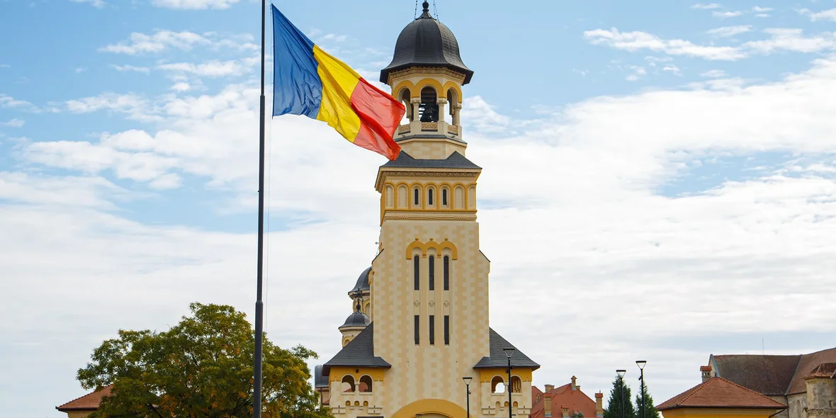 A picturesque view of the Romanian flag against the background of the Coronation Cathedral in Alba Iulia