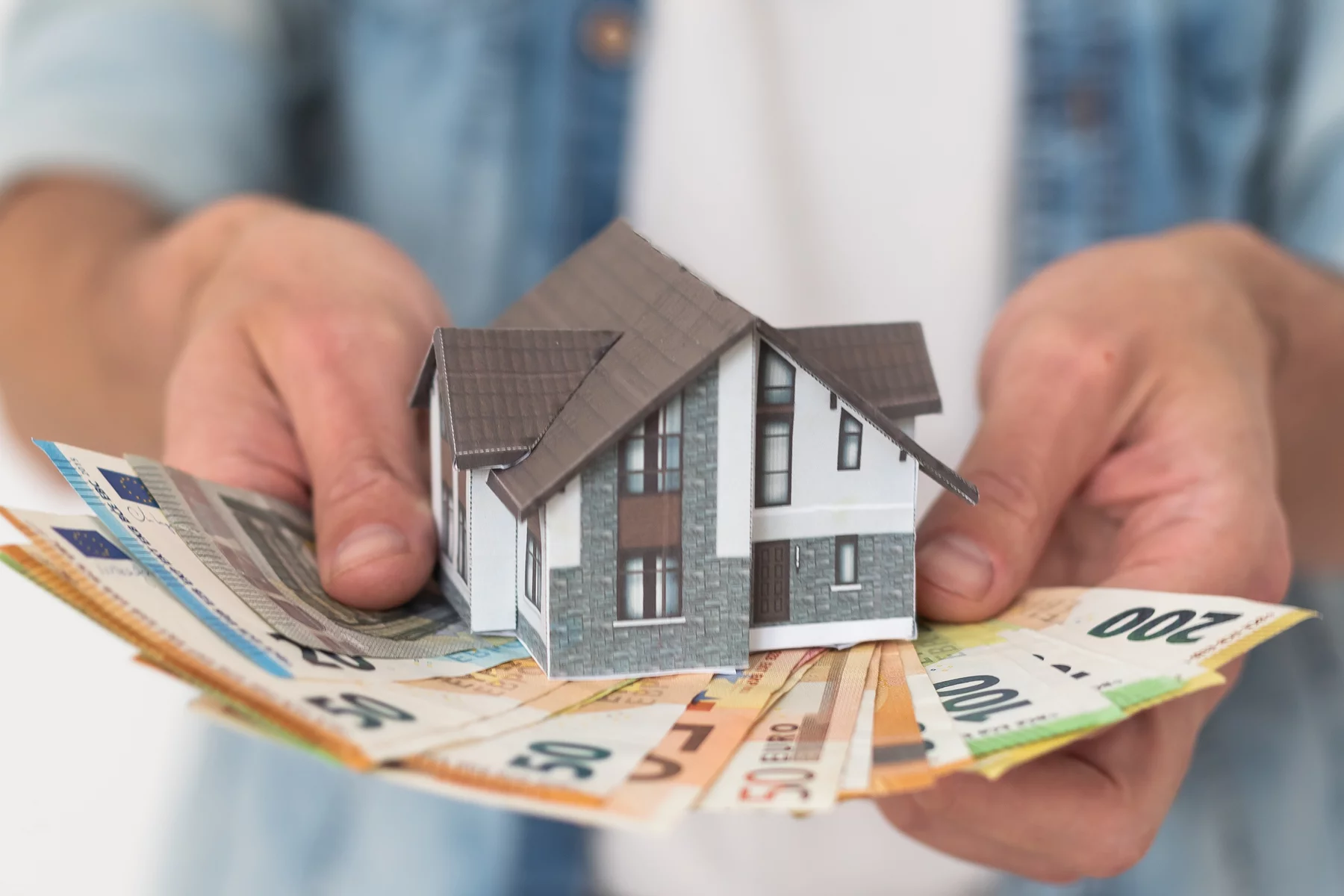 Покупатель недвижимости держит банкноты евро и модель дома