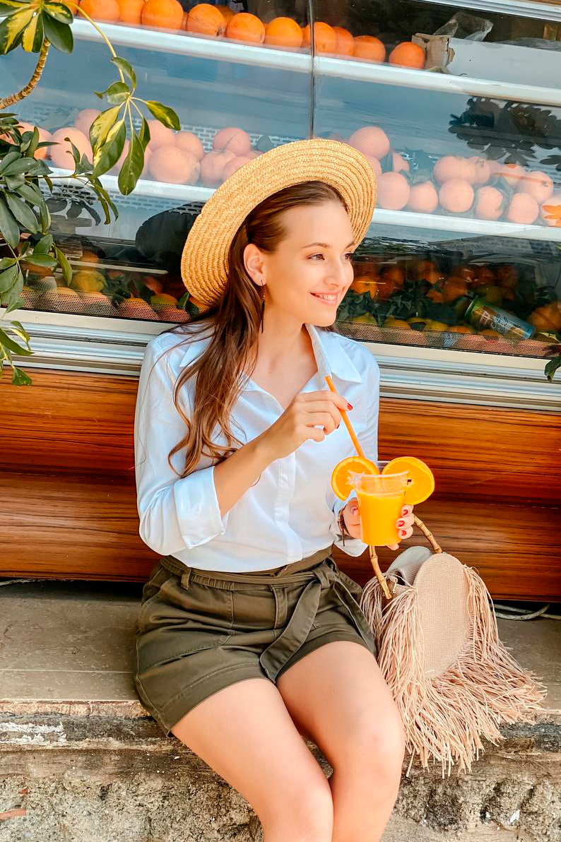 girl sits on the curb and drinks freshly squeezed juice
