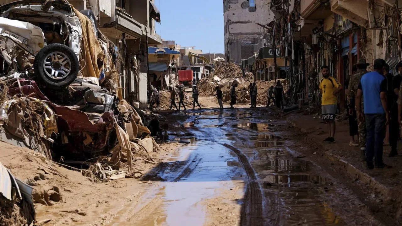 People walk near houses affected by flooding in Derna, Libya