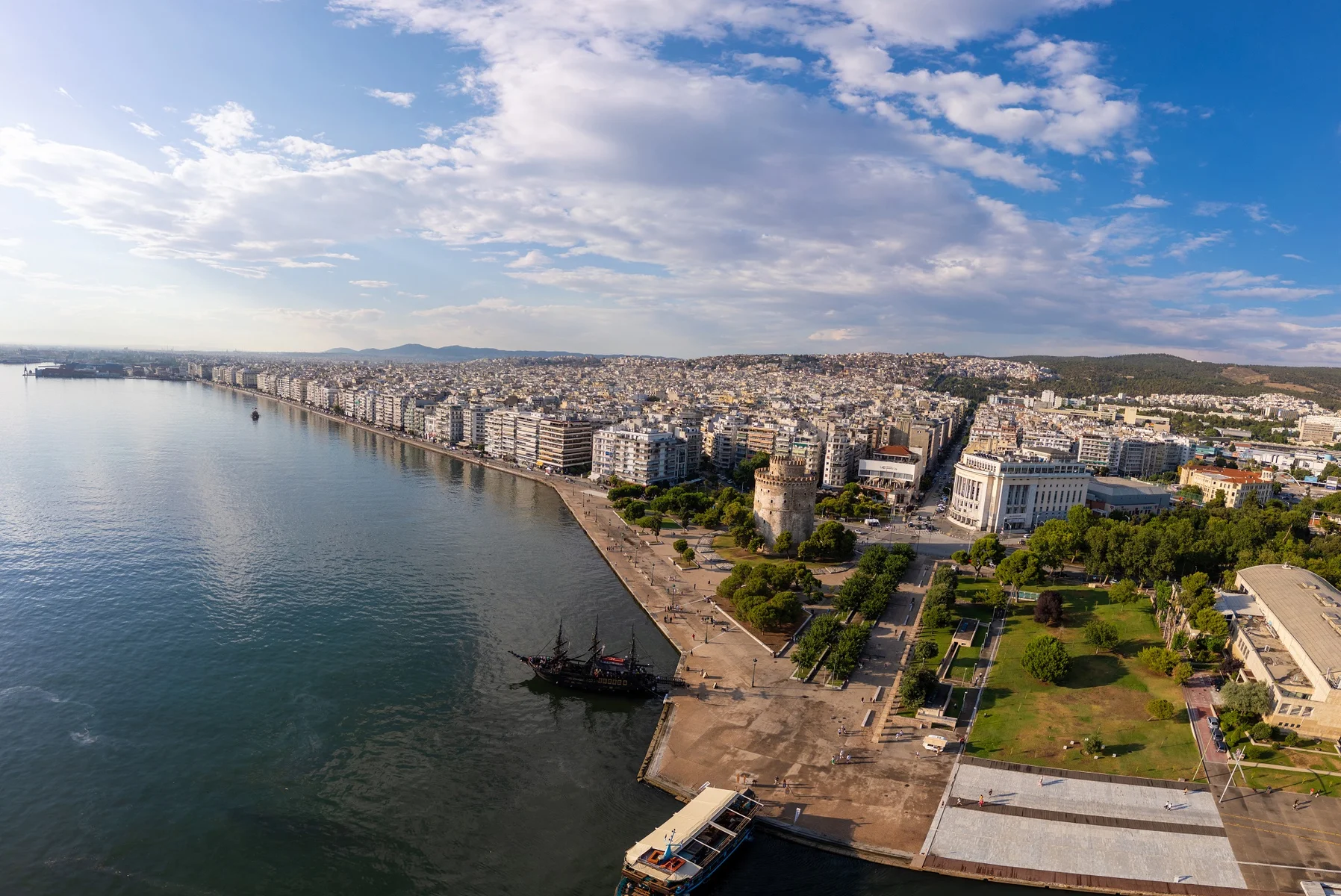 An aerial view of the White Tower in Thessaloniki, Greece, surrounded by lush greenery and colourful landscapes