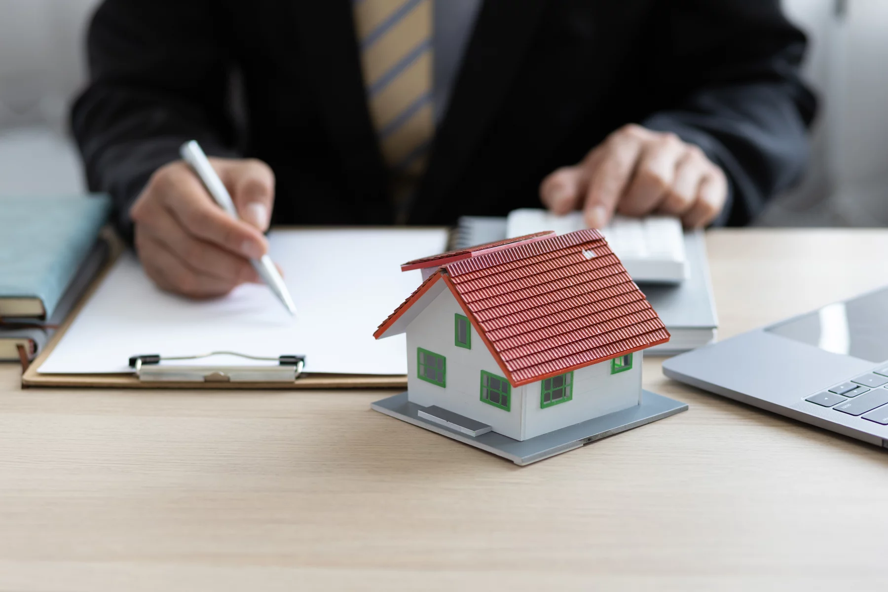un agente inmobiliario con una maqueta de una casa en las manos y papeles sobre su escritorio
